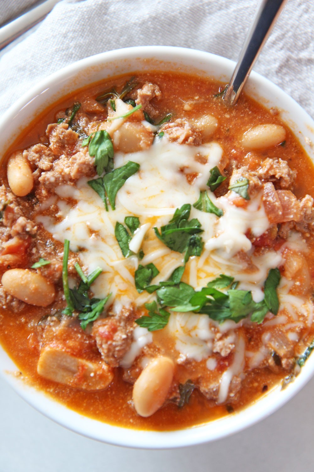 Cheesy Chicken Parmesan Chili Recipe. This is a healthy chili recipe. Quick one pot recipe that cuts the chicken parm cooking in half. Grab ground chicken, onions, garlic, red pepper, ricotta cheese, and more fun flavors. Happy dinner making! www.ChopHappy.com #chili #chickenparmesan 