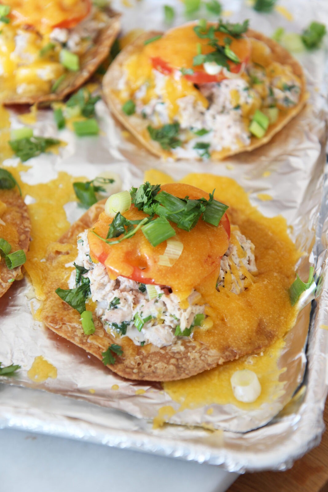 Tuna Melt Tostadas are so easy to make and are the perfect pantry dinner. Grab tortillas, tuna, mayo, cilantro, scallions, cheese, and lime. Happy Dinner cooking! www.ChopHappy.com #tostada #tunamelt